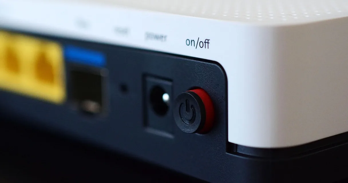 Botão liga e desliga vermelho na parte de trás de um aparelho branco, ilustrando como resetar a TV box